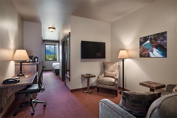 Interior guest room in Glacier National Park, featuring a desk, seating area, and wall-mounted TV.