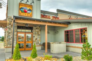 Exterior of a Glacier National Park restaurant with stone wall, wooden doors, and red-framed windows under a covered entry.