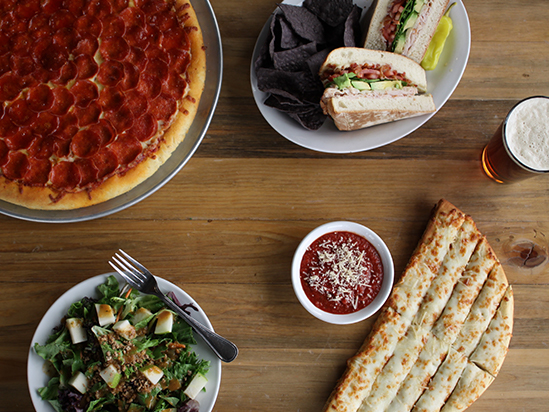 Inside a Glacier National Park dining spot, a pizza, salad, and flatbread spread on a wooden table.