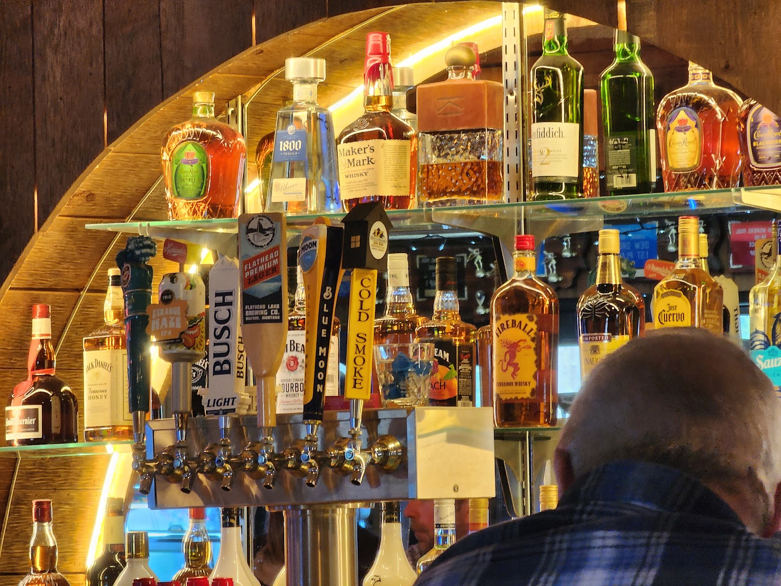 Bar interior at Glacier National Park featuring a row of liquor bottles and beer taps behind a wooden curved shelf.