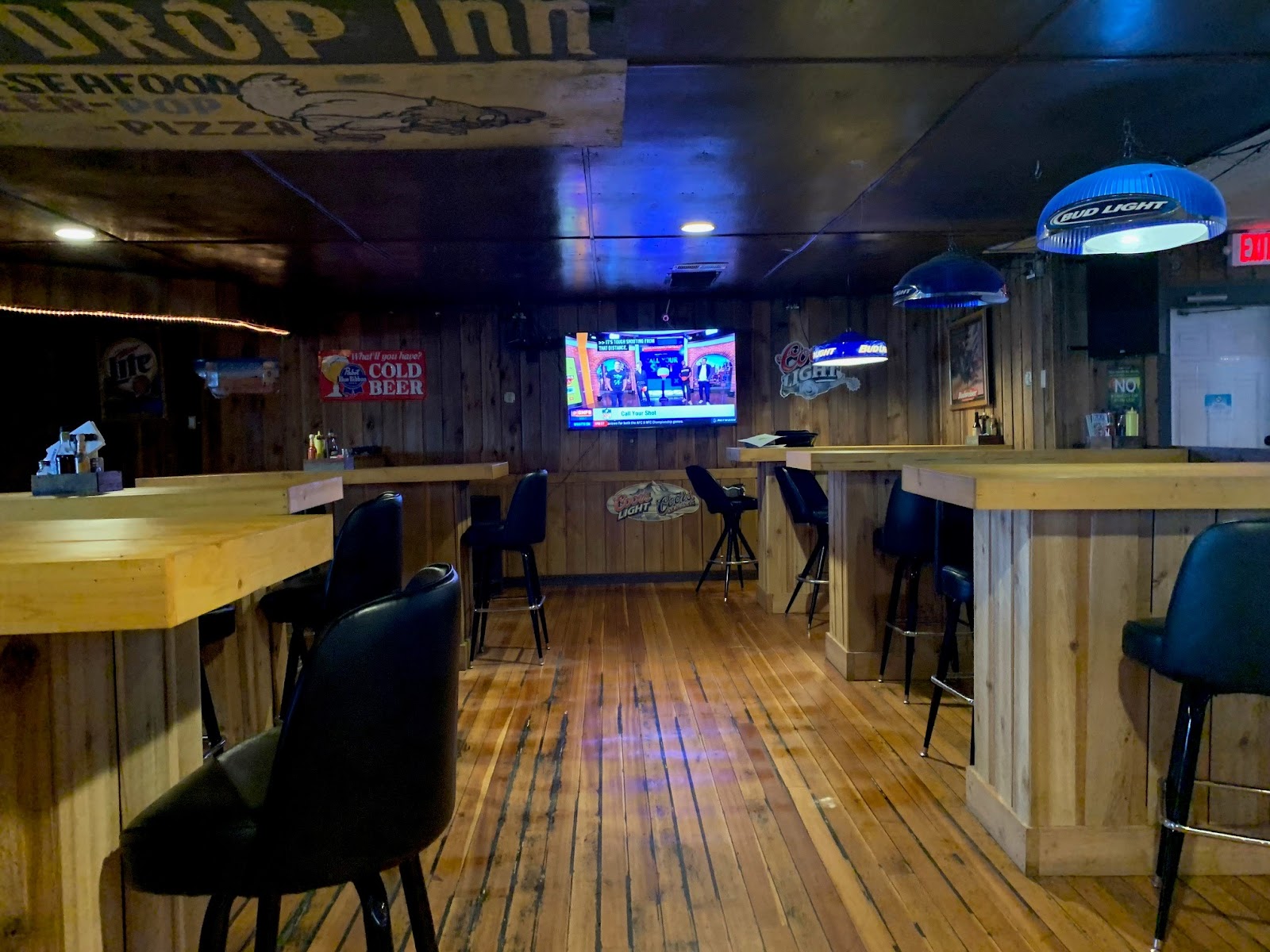 Interior of a rustic Glacier National Park bar with wooden countertops, stools, and a mounted TV.
