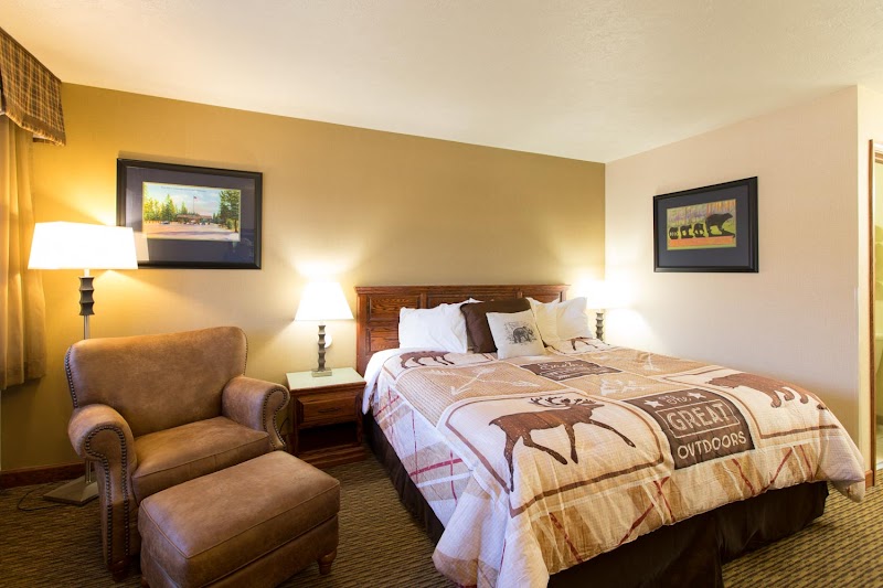 Cozy hotel room with a queen bed, two lamps, a chair and ottoman, framed landscape art, and a moose quilt in Yellowstone.