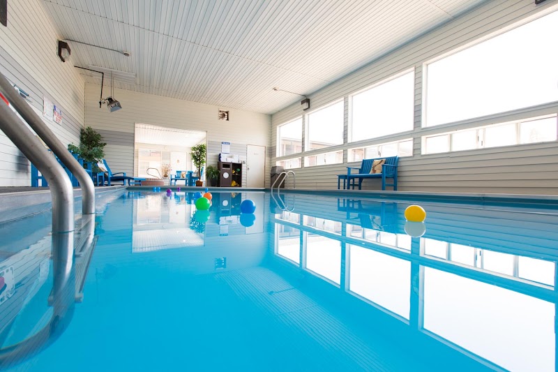 Indoor hotel pool with bright blue water, white paneled walls, large windows, blue lounge chairs, and colorful balls in Yellowstone National Park.