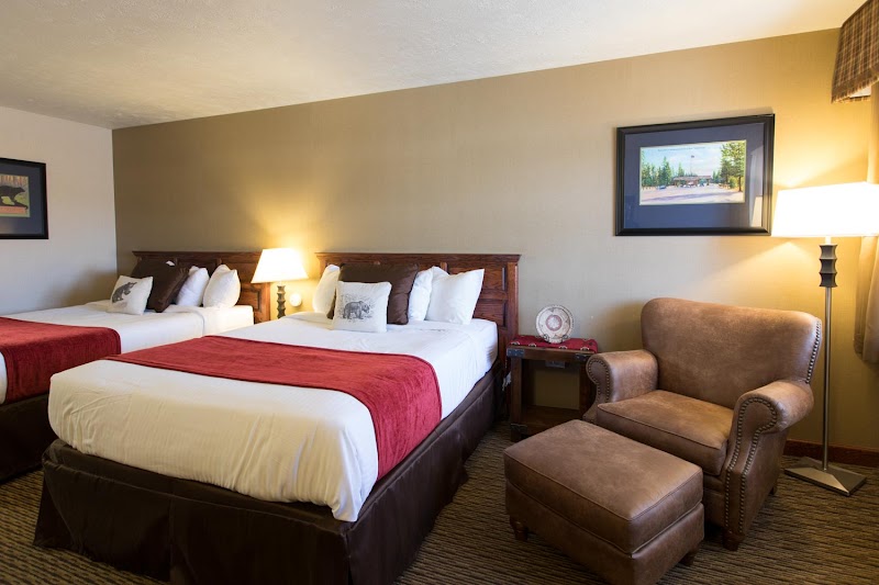 Two queen beds with white linens and red runners, brown furniture, and a chair with ottoman in Yellowstone National Park.