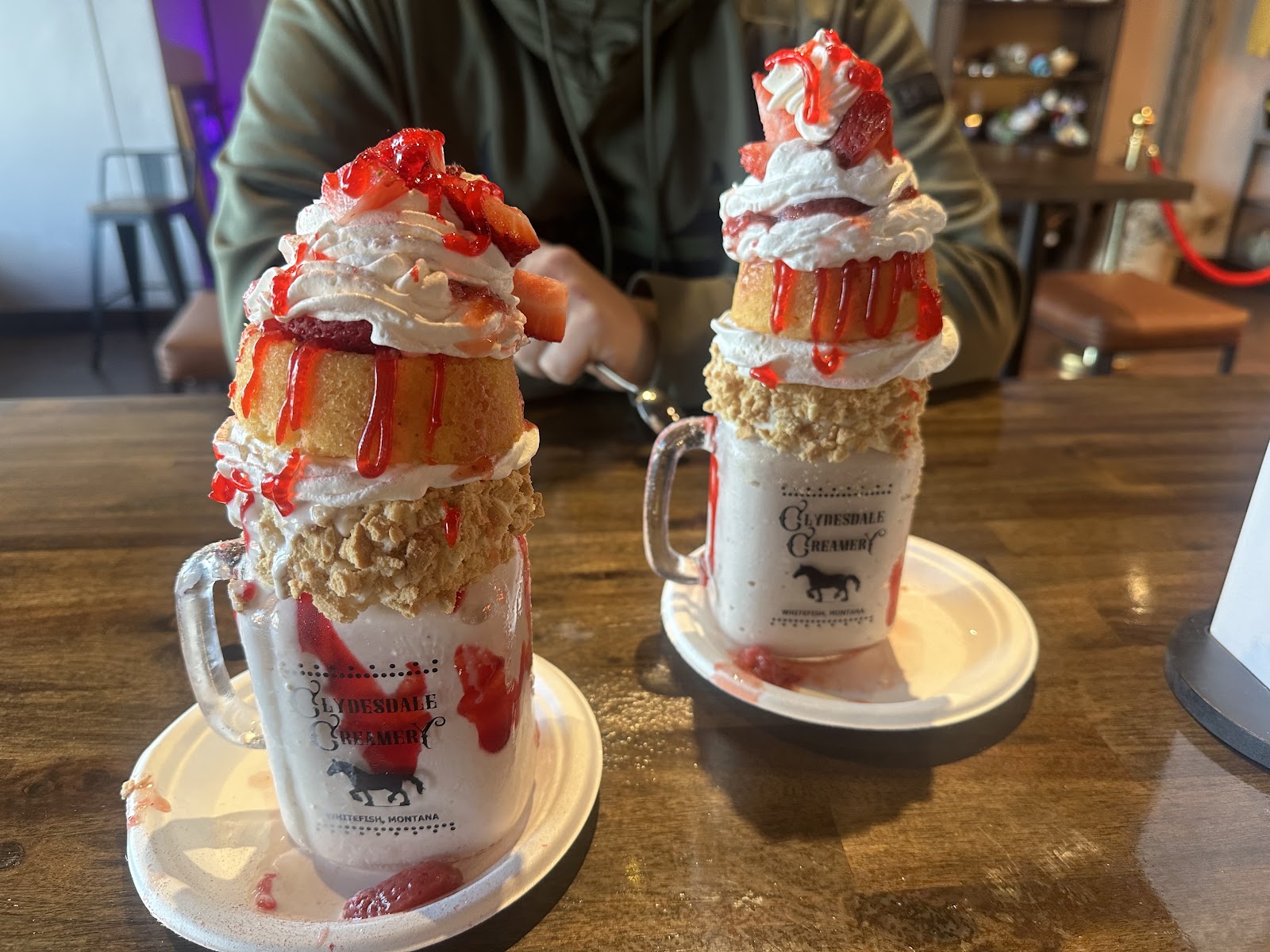 Two oversized whipped-cream topped milkshakes with strawberry drizzle and crunchy toppings at a Glacier National Park cafe.