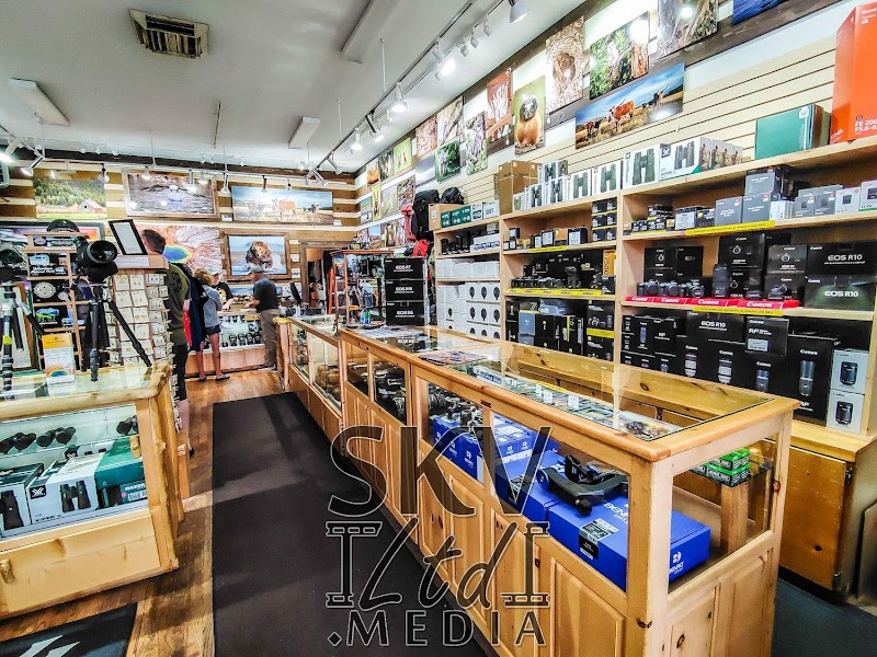 Inside a Yellowstone National Park gift shop, wood display cases line the aisle with cameras, lenses, boxes, and shelves of gear.