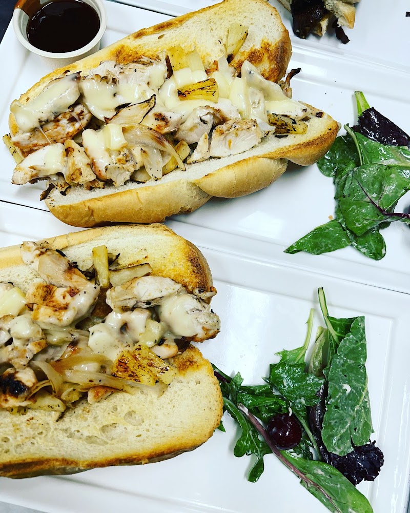 Grilled chicken, onions and melted cheese fill toasted bread, plated with greens on a white dish, in Yellowstone National Park.