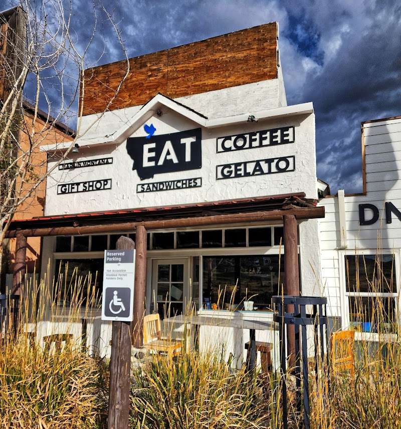 Yellowstone National Park cafe with white stucco facade, a large sign, and windows framed by tall grasses.