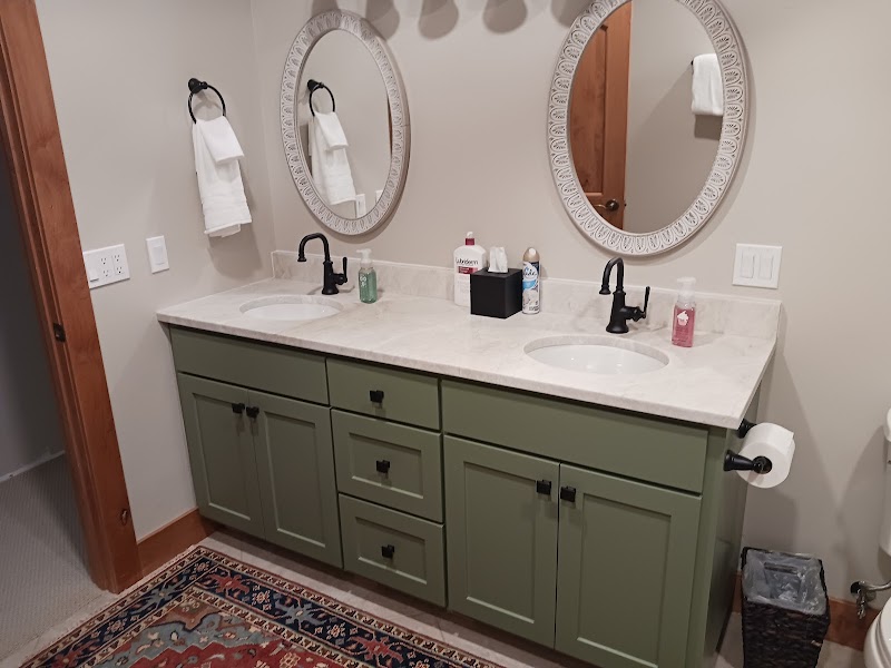 Dual-sink bathroom with sage green cabinets, marble countertop, two round mirrors and black faucets in Glacier National Park.
