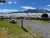 Grassy overlook with a wooden picnic table, benches, and a gravel path, facing snow-covered Yellowstone National Park mountains.