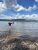 Person wading at Fish Creek Picnic Area along Glacier National Park’s shoreline with pebbled beach and blue sky.