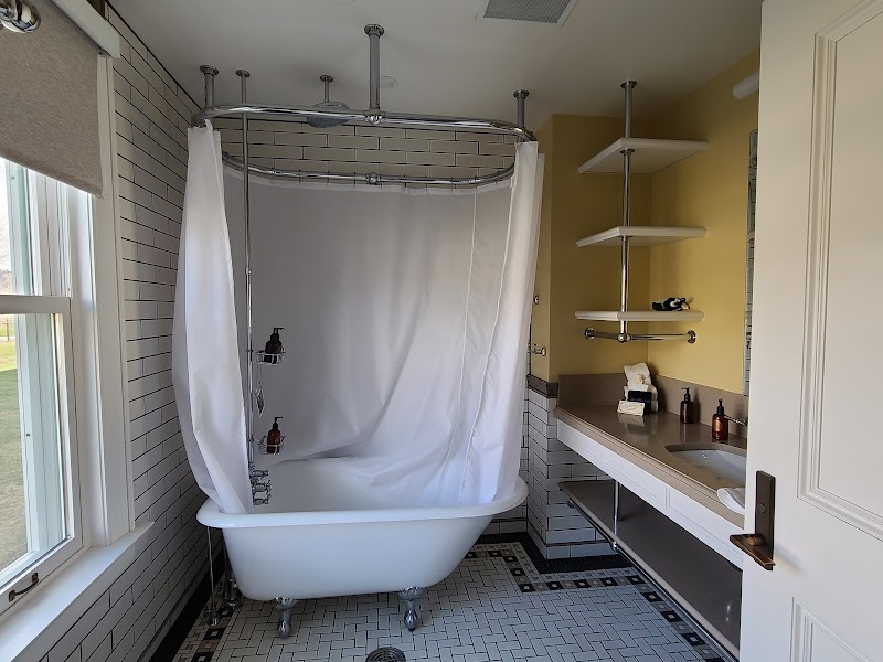 Bright bathroom with a white clawfoot tub, shower curtain, tile floor, and open shelves on a yellow wall in Yellowstone National Park.