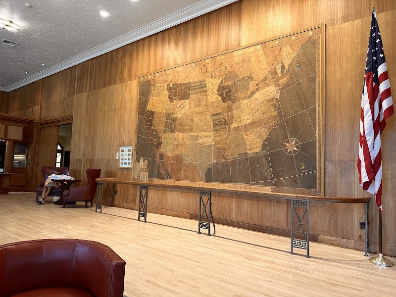 Interior lobby with a large vintage map on a wood-paneled wall, a long console table, an American flag, and a person reading in Yellowstone National Park.