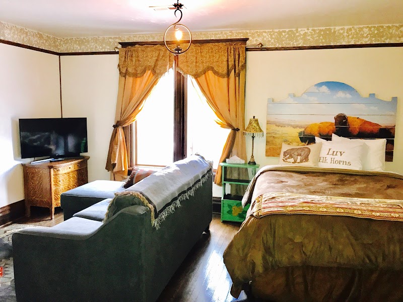 Cozy hotel room in Yellowstone National Park featuring a bed with a quilt, green sofa, mountain art, wood floors, and a TV.