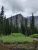 Snow-dusted peaks rise behind a dense evergreen forest and a shallow river at Twin Falls, Glacier National Park.