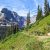 Hiker on Iceberg Lake Trail with rugged Glacier peaks overlooking a lush valley in Glacier National Park.
