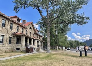 Yellowstone National Park visitor center building with stone walls and red roof lining a tree-lined walkway.