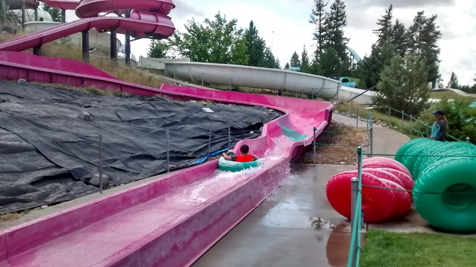 Pink twisting water slide at a family water park in Glacier National Park, with riders on tubes