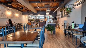 Spacious Fleur Bake Shop interior in Glacier National Park, featuring wooden tables, blue chairs, and warm pendant lighting for a cozy cafe vibe.