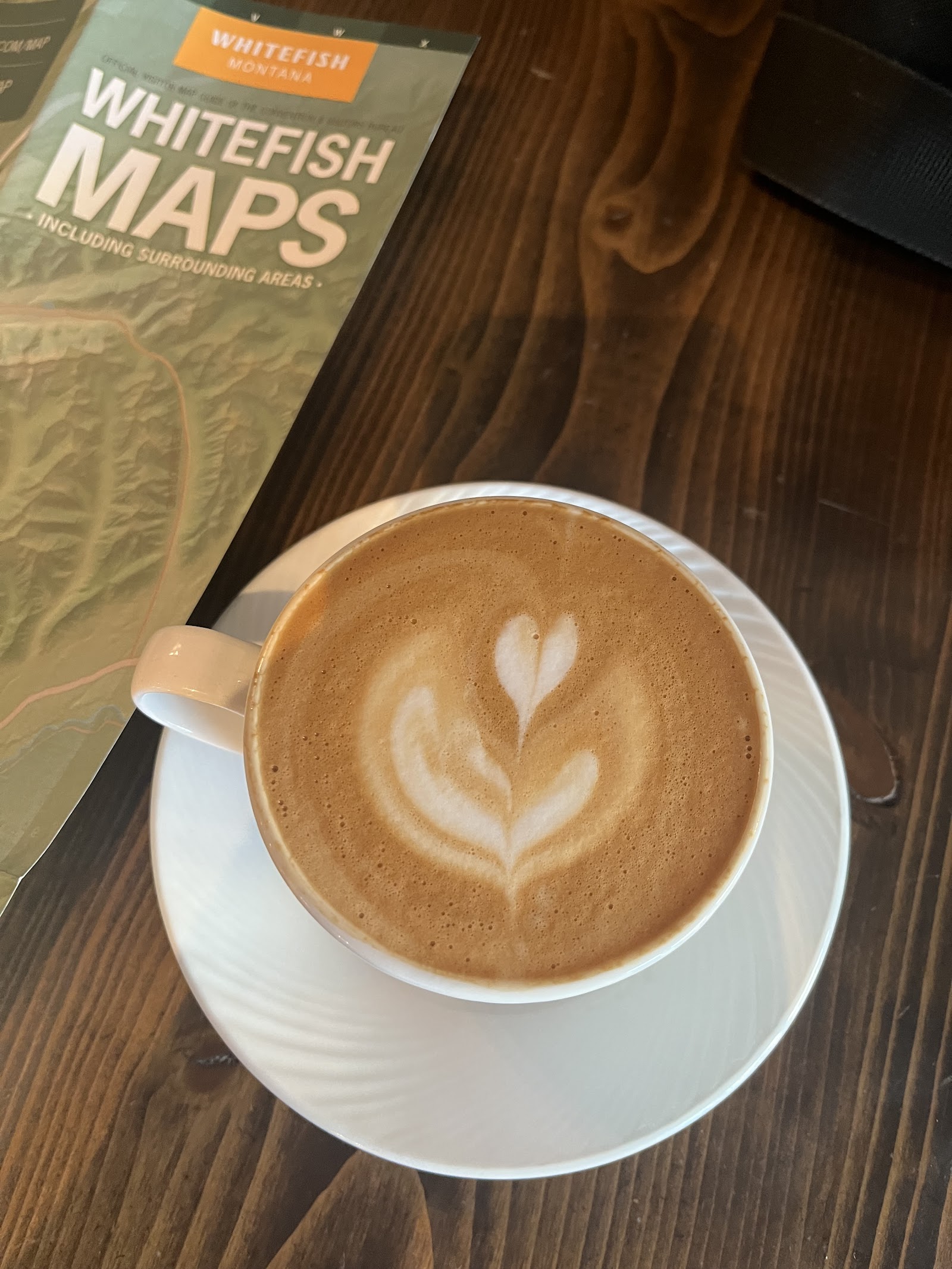 Creamy latte with fern-shaped latte art sits on a saucer in a cozy cafe inside Glacier National Park.