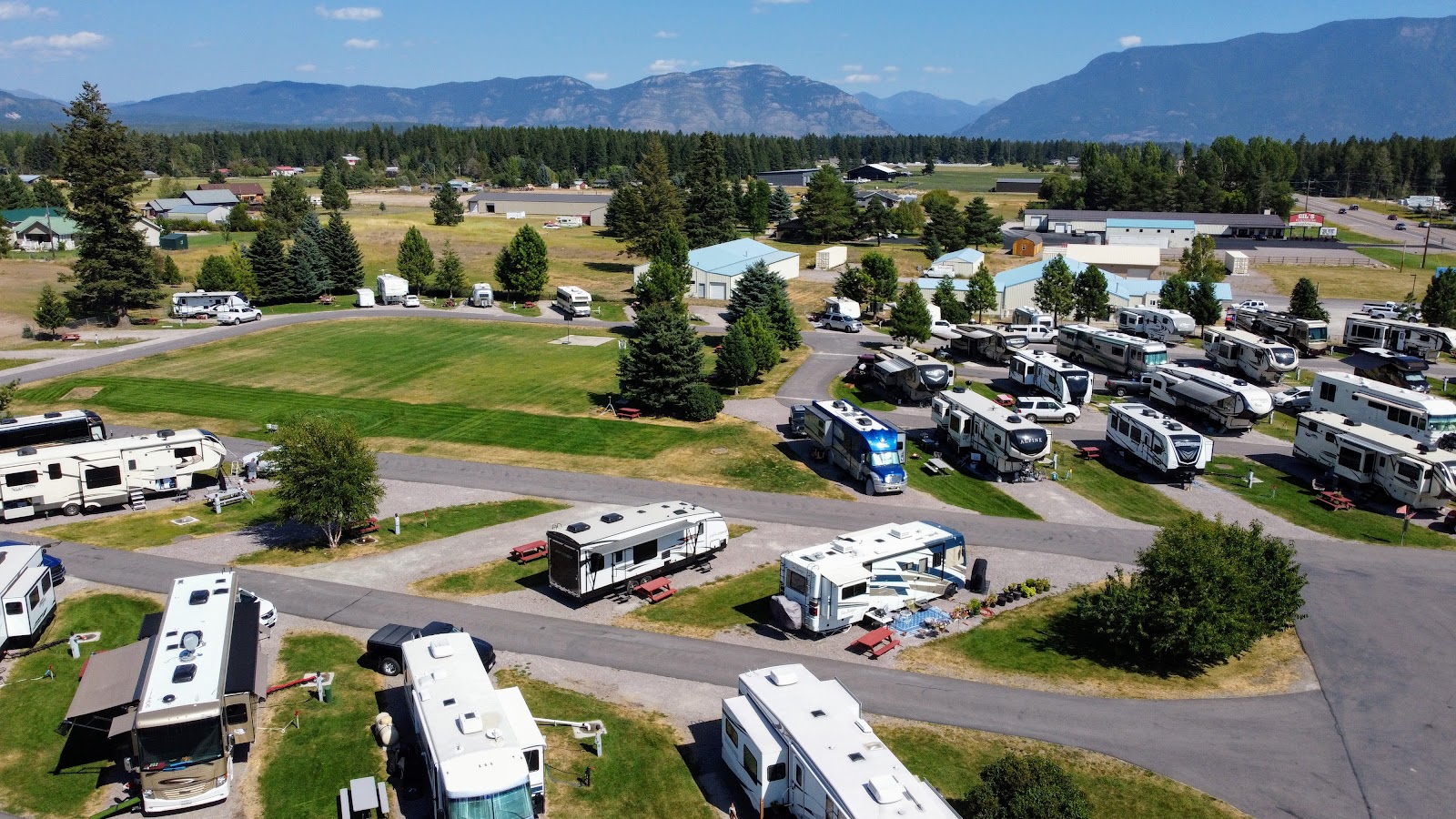 RV campground in Glacier National Park with numerous motorhomes parked along curving roads, green lawns, and tall pines.