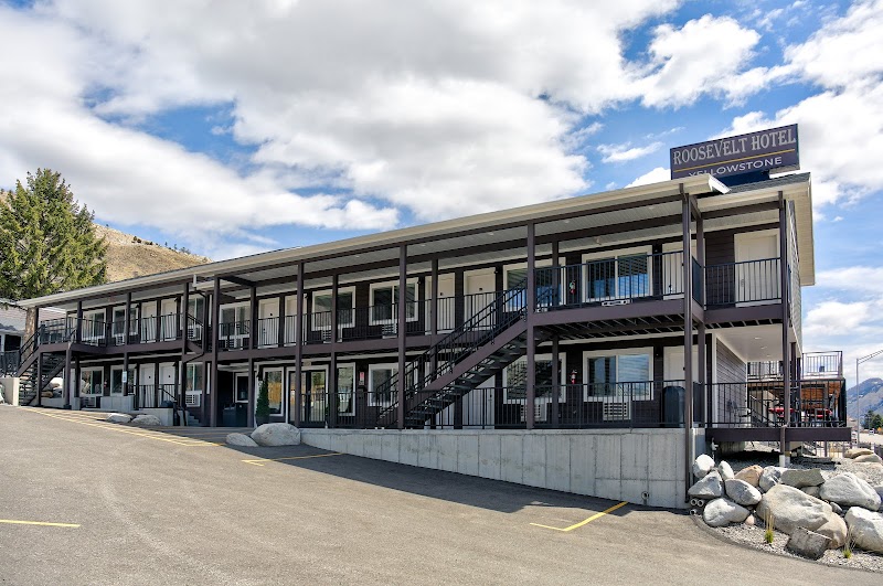 Two-story motel with exterior walkways and metal railings, staircases, and a front parking lot in Yellowstone National Park.
