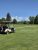 Cream golf cart with bags parked on a lush green fairway, pine trees and distant snow-capped peaks in Glacier National Park.