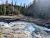 Rapid glacier-fed river crashes through layered rocky ledges in a forested canyon at Glacier National Park.