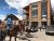 Horseback riders stroll past a rustic lodge along a Yellowstone National Park street.