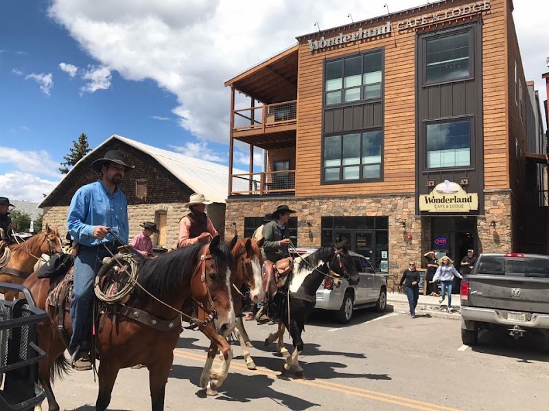 Group of riders on horses pass a two-story wooden lodge with a stone base in Yellowstone National Park.