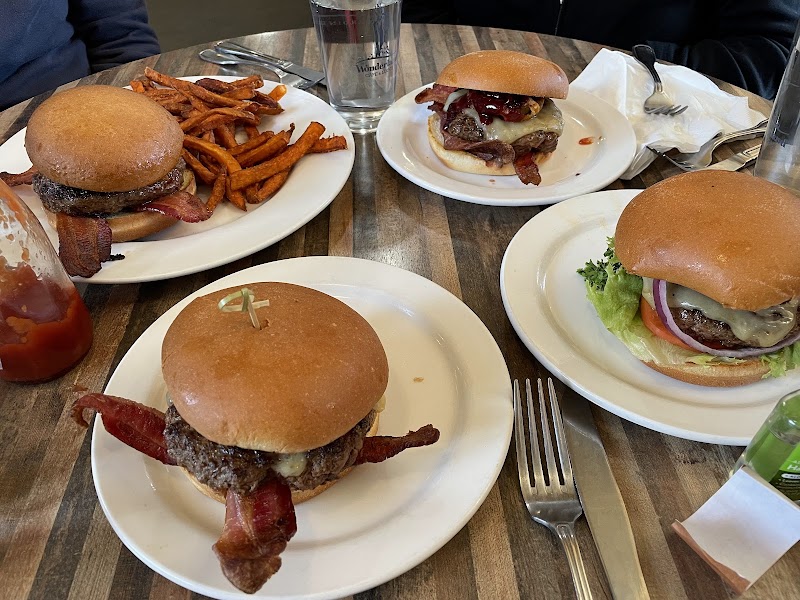 Three burgers with bacon and cheese on plates with fries on a wooden table in Yellowstone National Park.