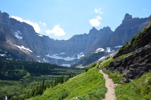 Iceberg Ptarmigan Trailhead in Glacier National Park climbs along a green slope with rugged peaks and patches of remaining snow.