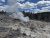 Steam rises from a geothermal vent over barren, rocky ground with dead trees near Yellowstone National Park.