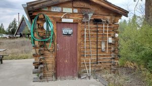 Rustic log shed at Yellowstone National Park campground; hoses, rakes, and shovels hung on the wall beside a weathered door.