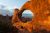 Sunset light bathes a large orange sandstone arch in Arches National Park, with jagged rock spires and blue sky beyond.