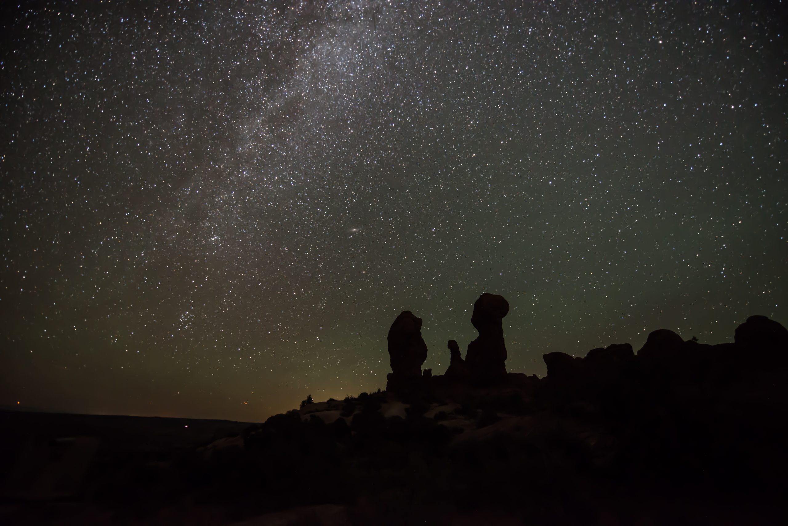 Star-filled night over Arches National Park with the Milky Way shining, silhouetted sandstone arches on the horizon.