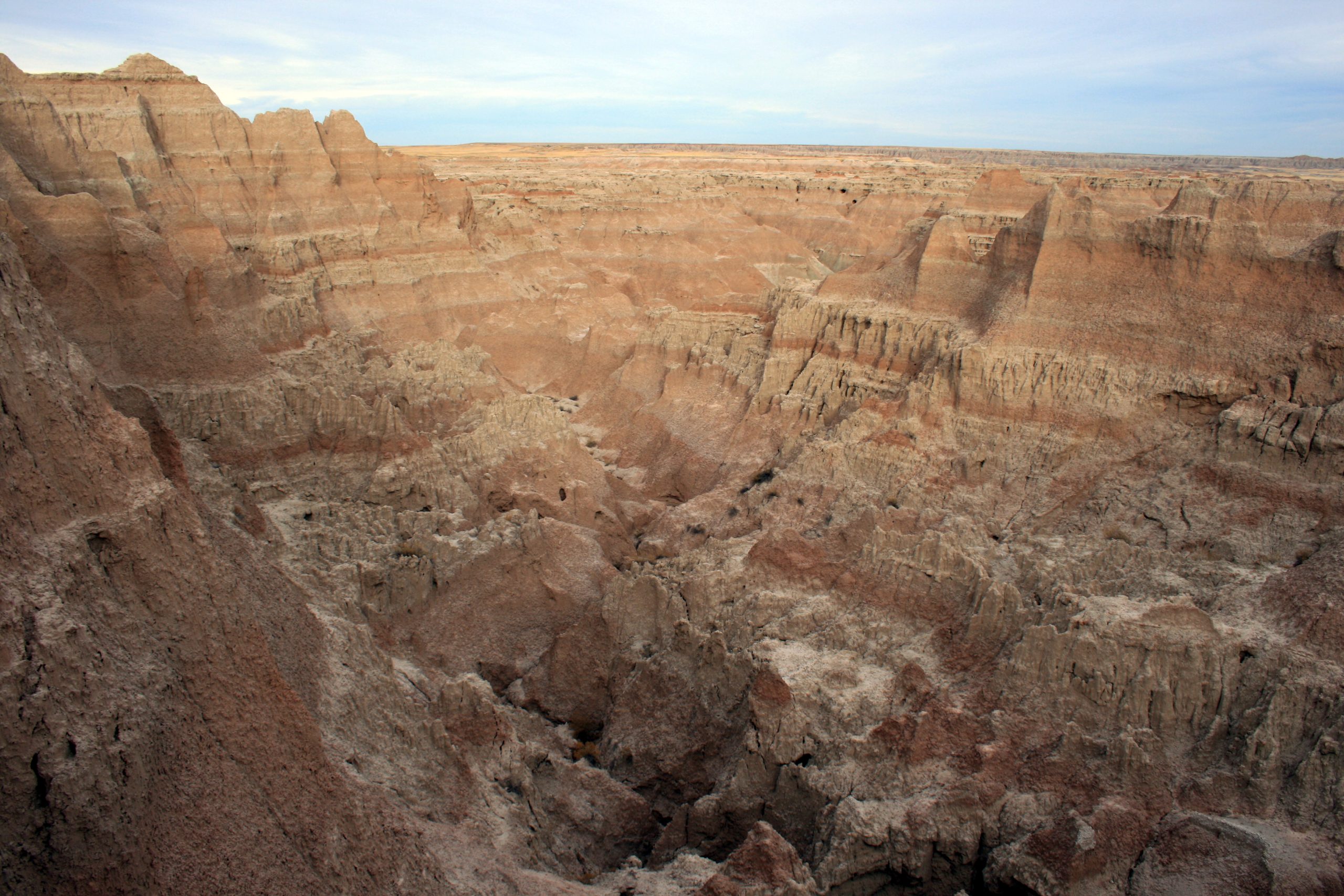 Rugged Badlands National Park badlands with red-brown layered cliffs and deep ravines under a pale blue sky.