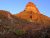 Red rock formation rises over rugged desert slopes in Big Bend National Park at golden hour.