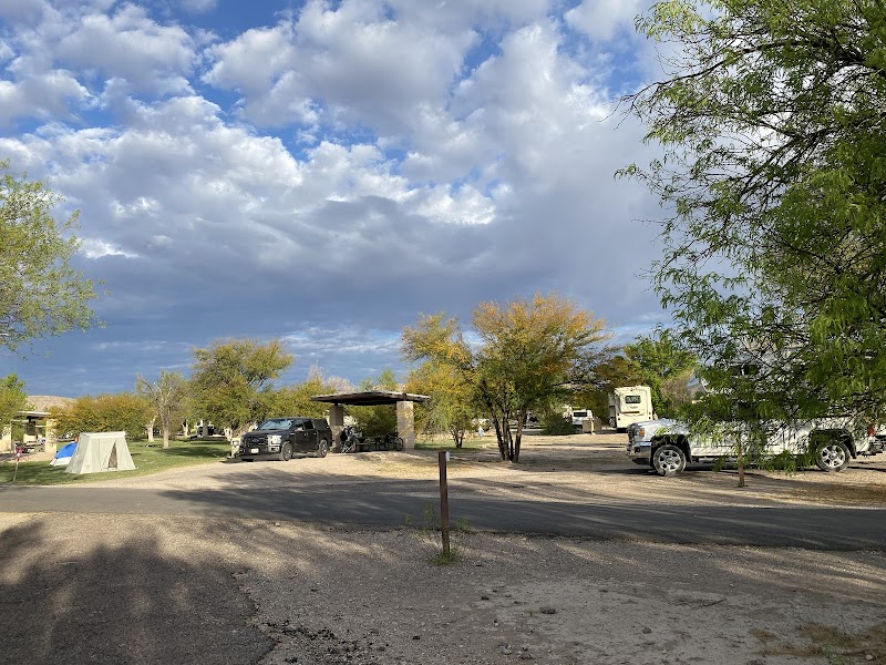 Camping scene at Rio Grande Village Campground in Big Bend National Park, with tents, RVs, and scattered trees under a partly cloudy sky.