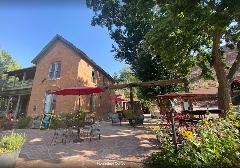Outdoor cafe seating at Horsethief Coffee in Arches National Park, a brick building with red umbrellas and a sunny courtyard.
