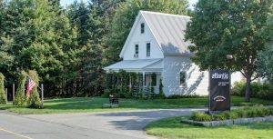 White two-story house with a metal roof, front porch, green lawn, flagpole, and a roadside sign in Acadia National Park.