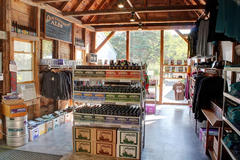 Inside a rustic shop at Acadia National Park, shelves stock beer boxes, bottles, T-shirts, and souvenirs with natural light.