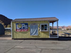 Small yellow concession hut with a metal roof and open porch at Arches National Park, desert flat, red rock hills in the distance.