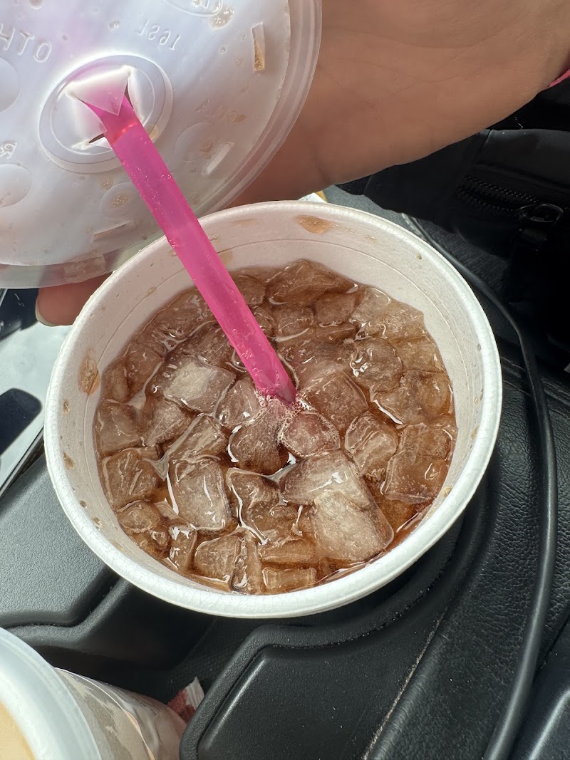 Cold iced drink with pink straw in a foam cup, held by a hand inside a car at Arches National Park over ice cubes.