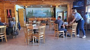 Rustic restaurant dining room in Acadia National Park with wooden walls and a lakeside mural in the back.