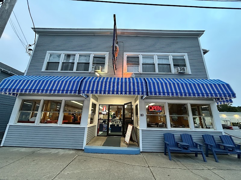 Two-story storefront with striped awning, open door, neon OPEN, and blue Adirondack chairs outside in Acadia National Park.