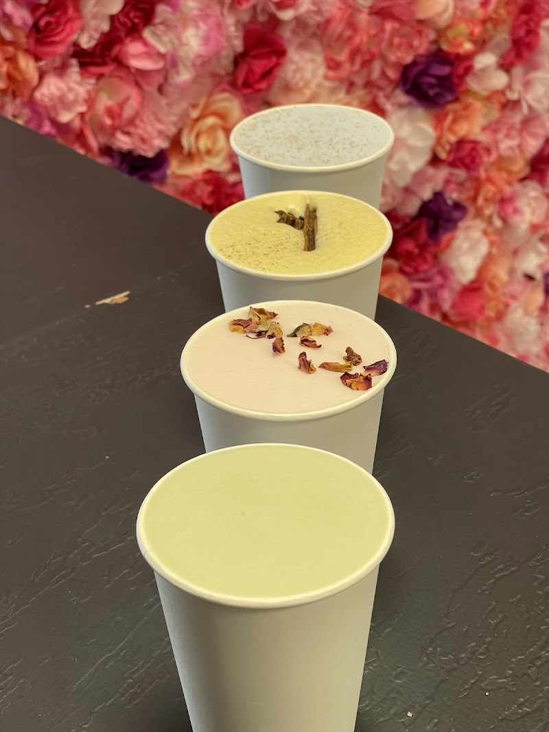 Pastel drinks in five white cups line a dark counter, topped with petals or a cinnamon stick, against a pink floral wall at Arches National Park.