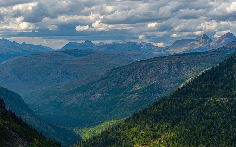 Vulture Peak overlook view in Glacier National Park showing green valley and layered mountain ridges under a cloudy sky.