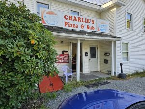 Pizza shop storefront in Acadia National Park area with a Coca-Cola sign and a purple plastic chair outside.
