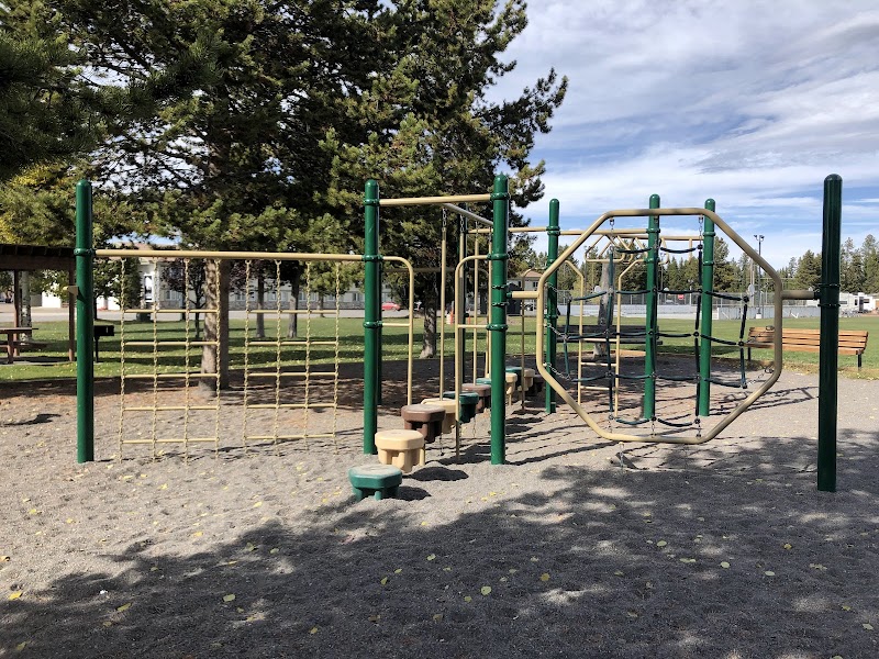 Playground with green metal climbing structures, rope nets, and stepping stools in West Yellowstone Heritage Park, Yellowstone National Park.